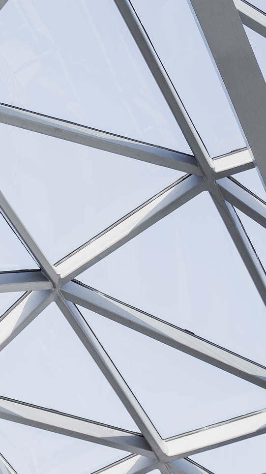Stahlgitterkonstruktion aus silbergrauen Trägern, die sich in einem präzisen Winkel kreuzen und Glasfenster fassen.